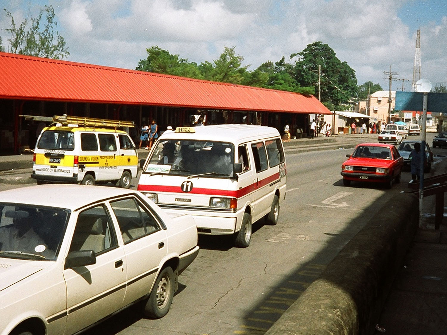 „Innenansicht eines ZR Vans in Barbados. Enge Sitzreihen, farbige Rückenlehnen und handgemalte Schriftzüge prägen den Raum. Der Blick richtet sich nach vorne durch das Fahrzeug und vermittelt Nähe, Enge und die gemeinsame Erfahrung von Bewegung im öffentlichen Transport.“